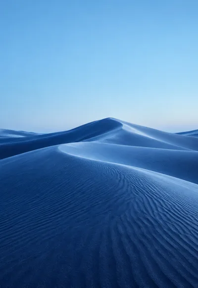 Powder-blue dune crests flow into indigo shadows beneath an open sky.