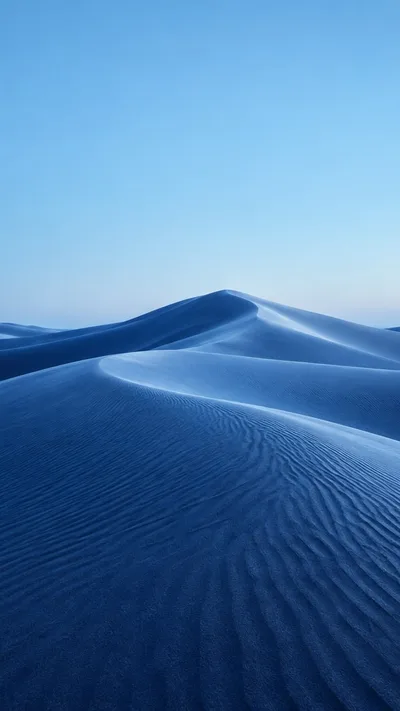Powder-blue dune crests flow into indigo shadows beneath an open sky.